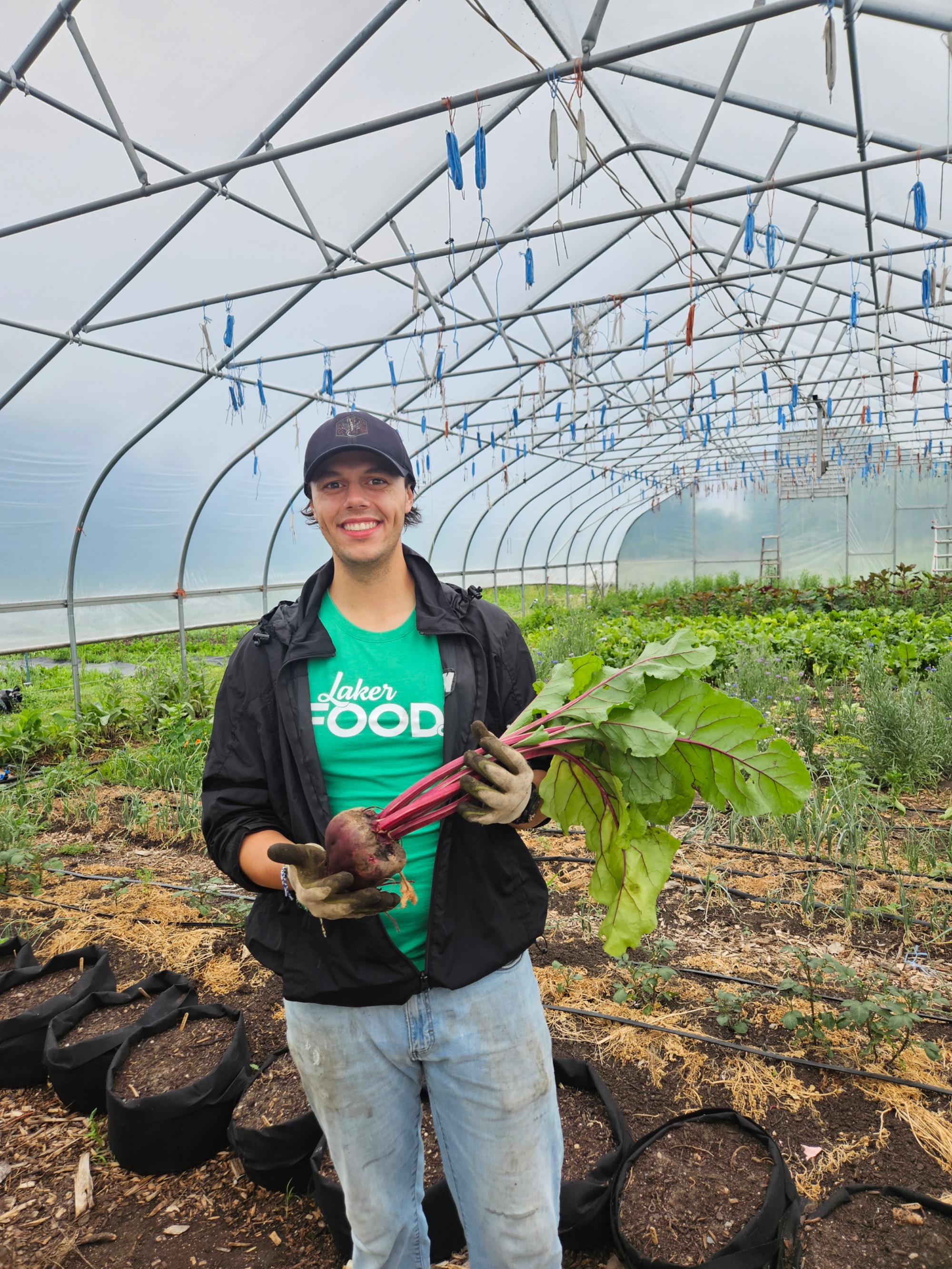 Green Team Student at Sustainable Agriculture Project farm holding beet inside greenhouse